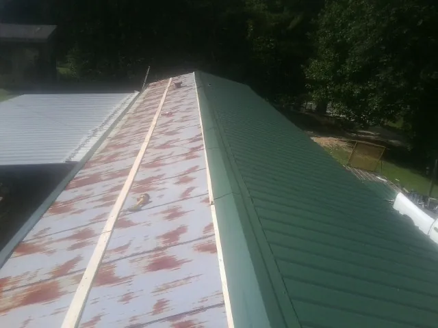 Old rusted panels beside newly installed green metal roofing — Wind Damage Roof Repair by Roofing Brothers in Maxwell